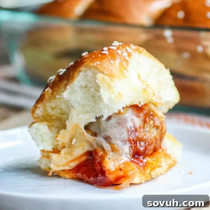 Effortless Tangy Meatball Sliders 5 Meatball slider with melted cheese and sauce on a sesame bun, placed on a white plate.