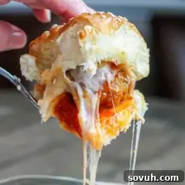 Hand holding a meatball slider with marinara sauce and melted cheese, pulling away to reveal stretchy cheese strands.