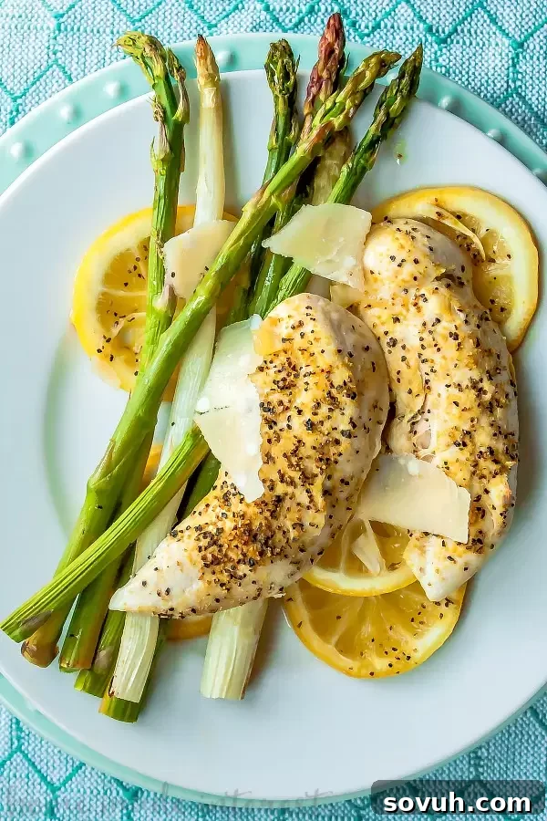 A plated serving of sheet pan chicken and asparagus, garnished with fresh Parmesan shavings and herbs