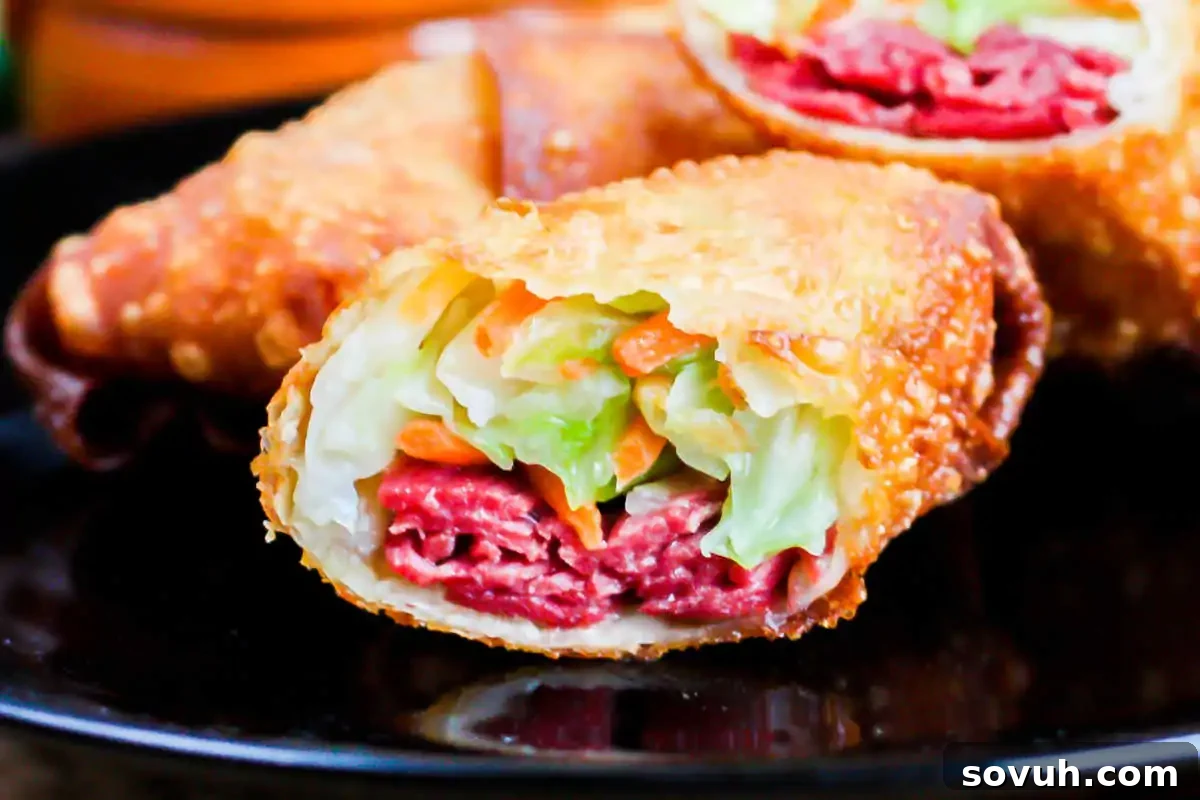 Close-up of a golden-brown Irish egg roll, halved to reveal a savory filling of shredded cabbage, carrots, and tender corned beef, served on a dark plate.
