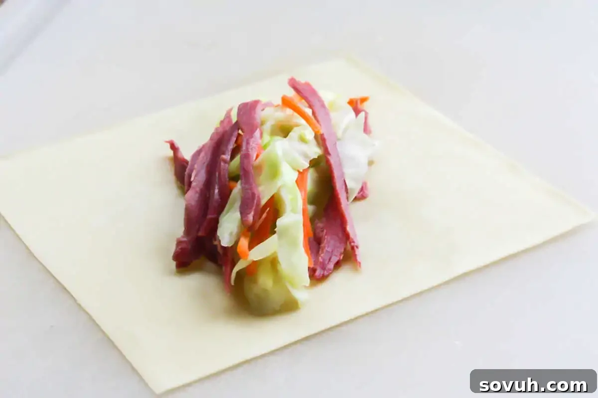 Unrolled egg roll wrapper showcasing a vibrant filling of sliced corned beef, shredded cabbage, and carrots, perfectly prepped for rolling.
