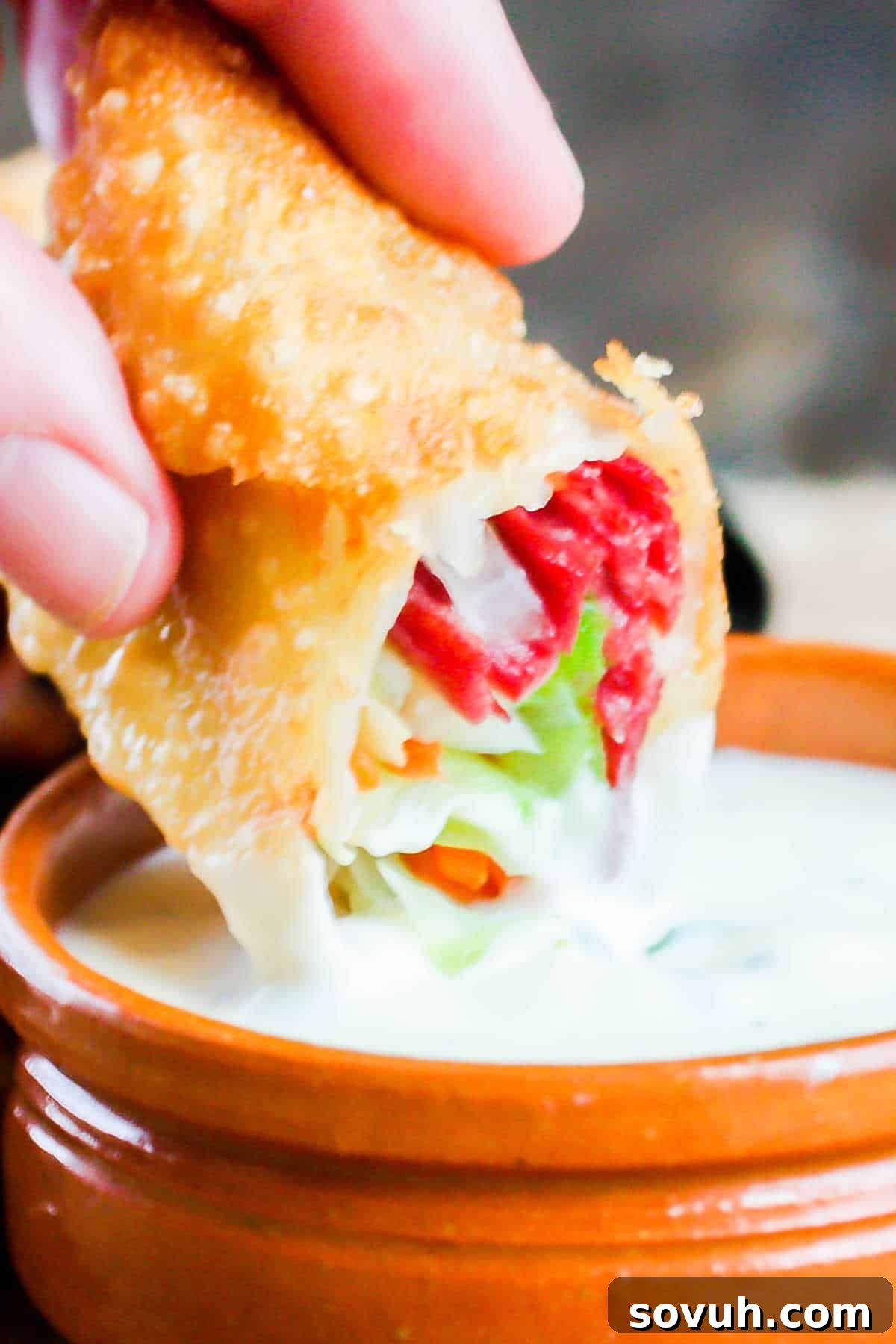 A hand dipping a golden-fried Irish egg roll into a small bowl of creamy parsley mustard sauce, highlighting the perfect appetizer for St. Patrick's Day.