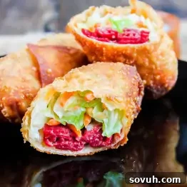Close-up of crispy corned beef egg rolls cut open to reveal a filling of bright red meat, shredded lettuce, and carrots on a black plate.
