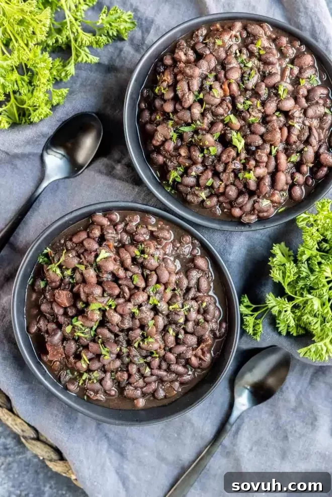 Two black bowls brimming with delicious Instant Pot Black Beans, presented side-by-side on a rustic wooden table.