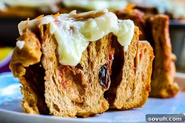 Close-up of a warm Carrot Cake Cinnamon Roll, revealing its moist interior and luscious cream cheese frosting.