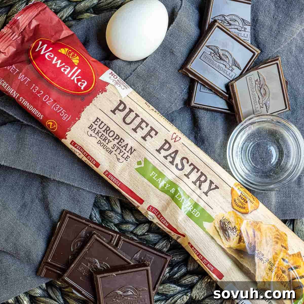Ingredients laid out for Easy Chocolate Croissant recipe: puff pastry, dark chocolate bars, egg, and a small bowl of water.