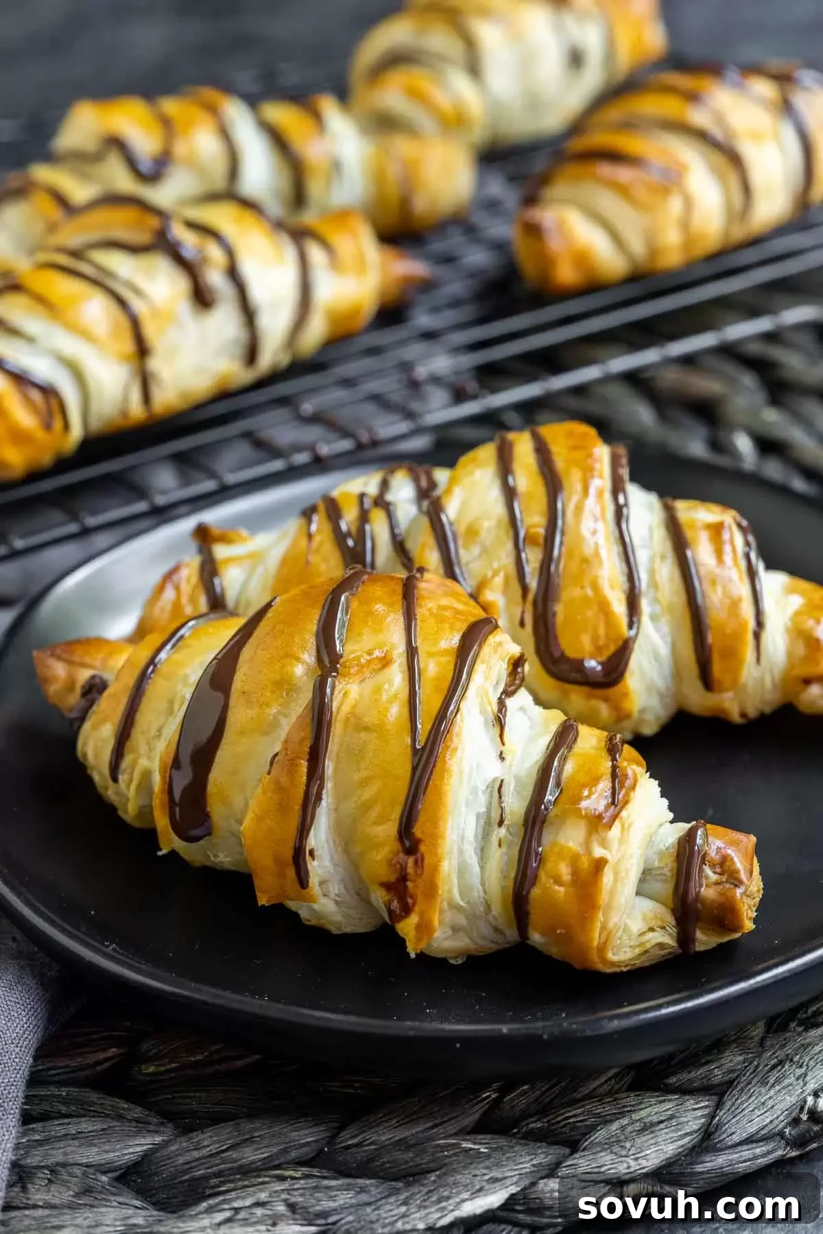 Two easy chocolate croissants on a black plate, with more in the background
