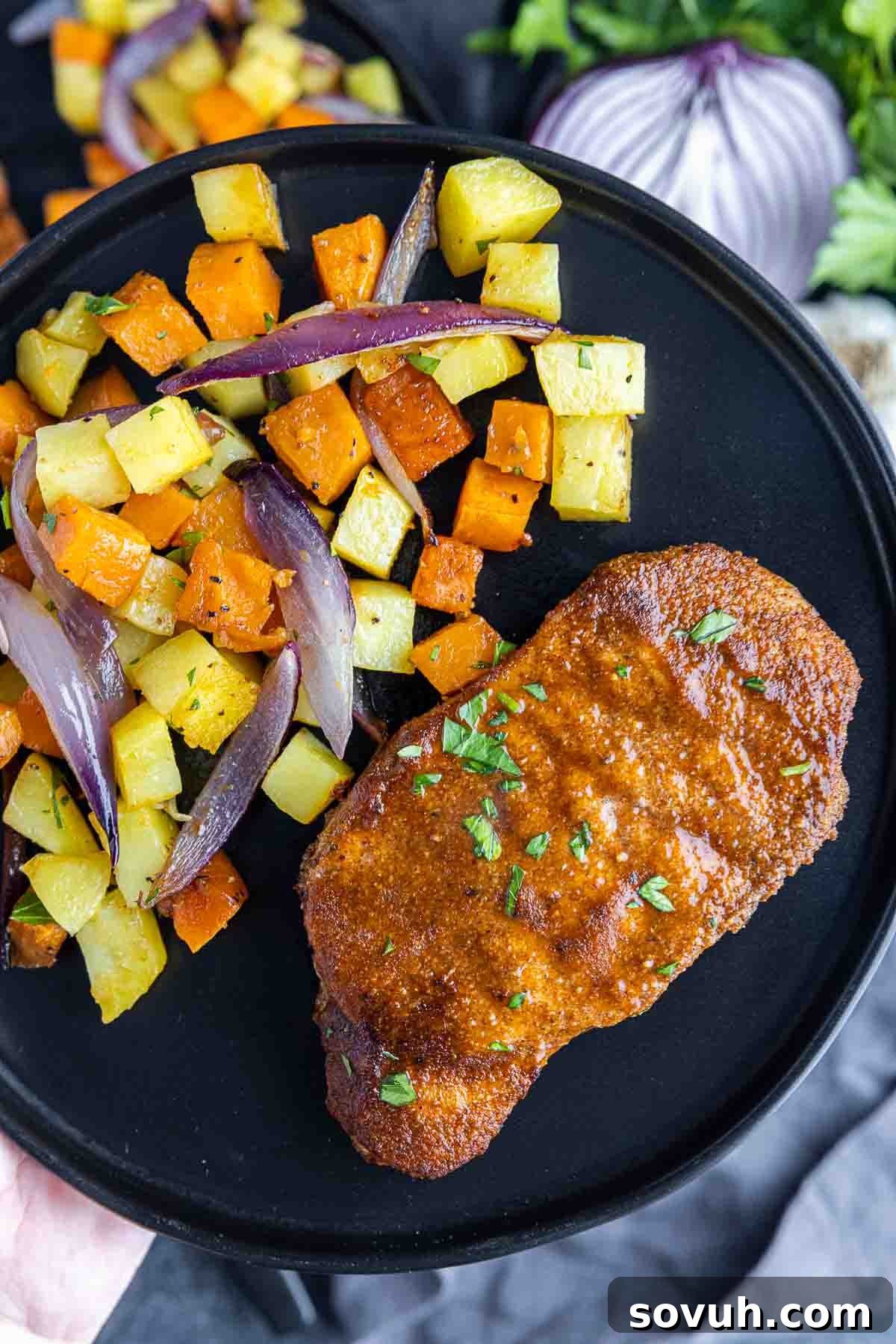 A hand presenting a black plate with a beautifully plated Sheet Pan Spicy BBQ Pork Chop and roasted potatoes, garnished with fresh cilantro.