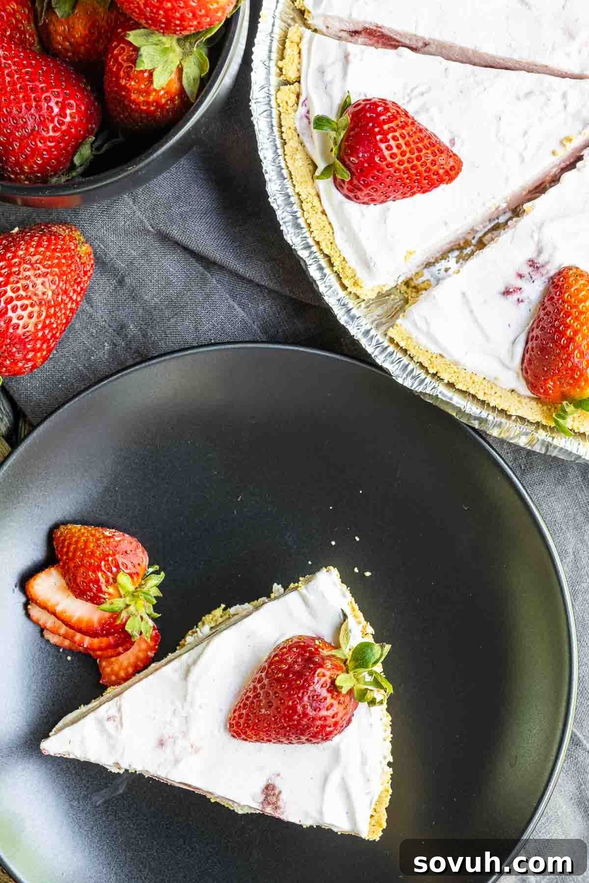 Slice of Frozen Strawberry Pie on a plate with whole pie next to it, garnished with fresh strawberries