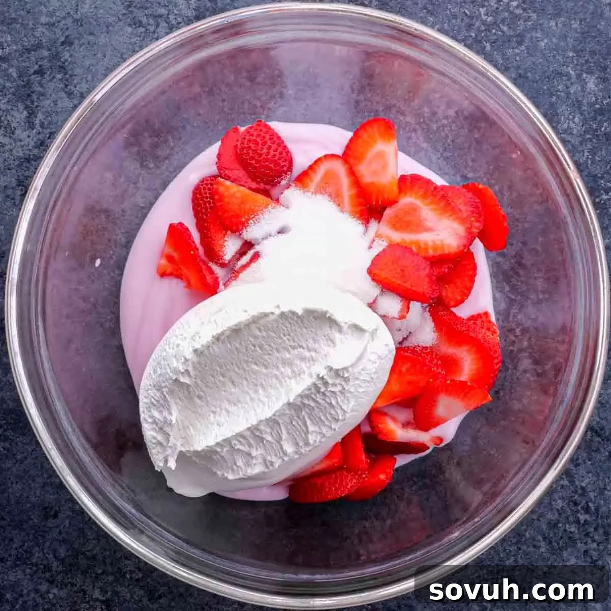 A bowl of strawberry yogurt with whipped cream and strawberries, ready to be mixed.