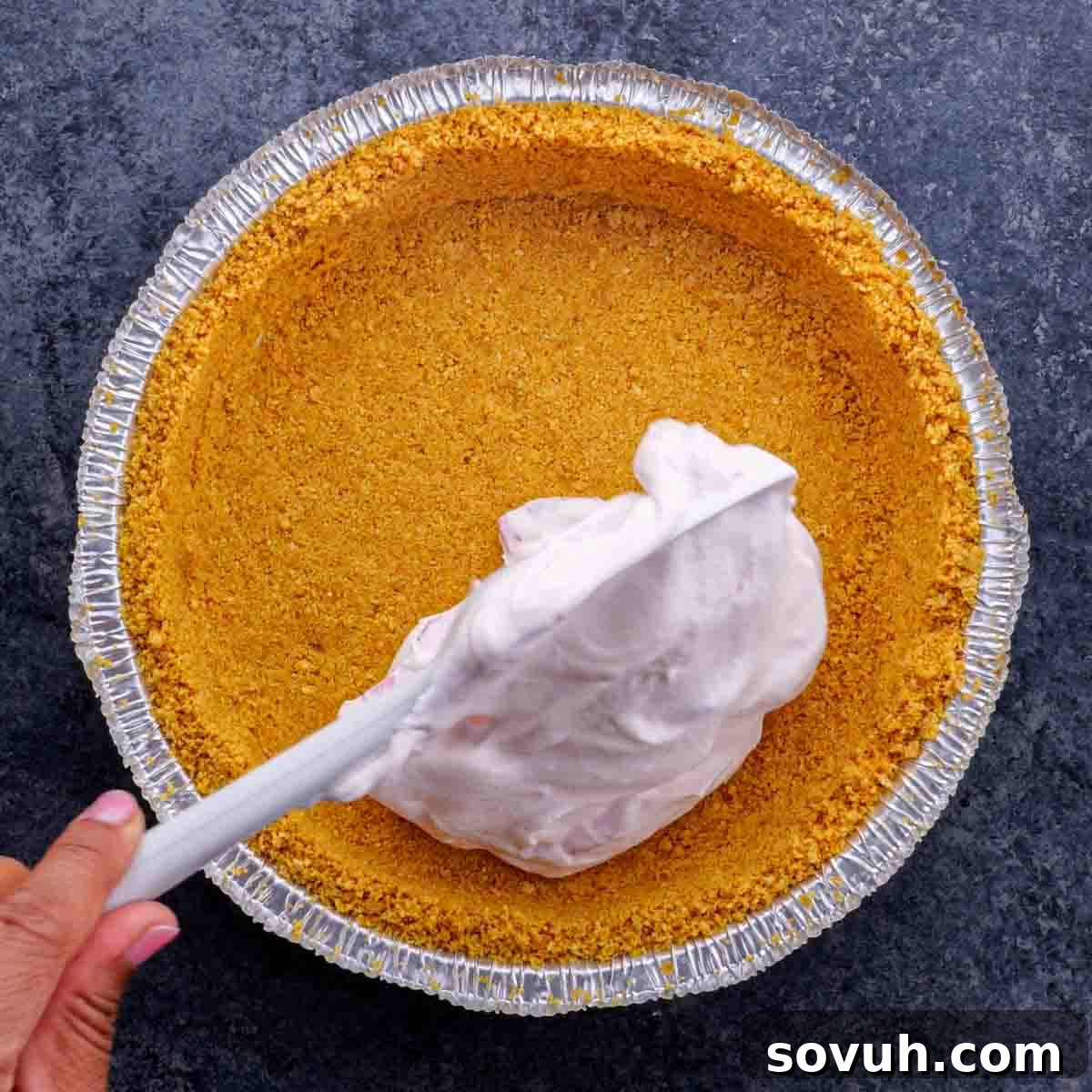 A person pouring strawberry pie filling into a pie crust, showing the consistency of the filling.