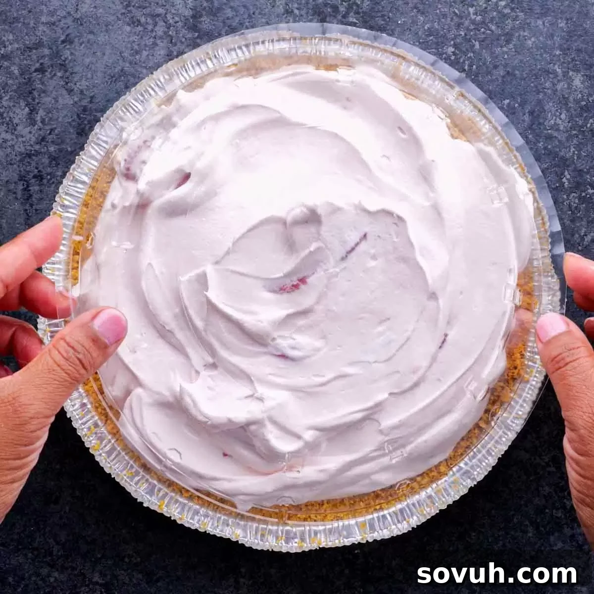 A person holding a frozen pie with strawberry filling, demonstrating it's ready for freezing.