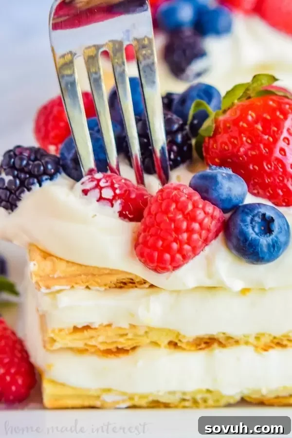 A slice of Lemon Berry Napoleon with a fork, showing the defined layers of pastry and mousse, ready to be enjoyed.