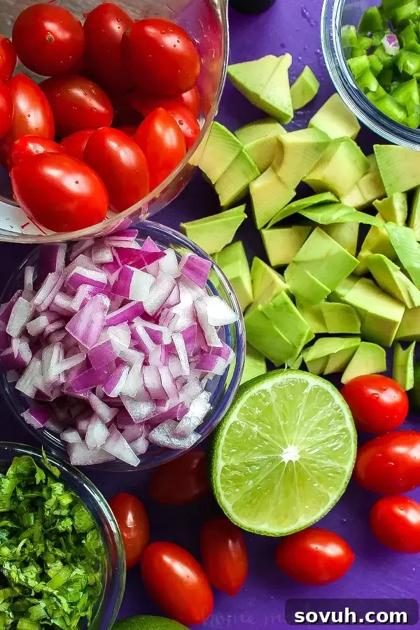Ingredients for Mexican Pasta Salad, including multi-colored pasta, roasted corn, black beans, cherry tomatoes, green peppers, red onion, avocados, cilantro, queso fresco, and dressing components.