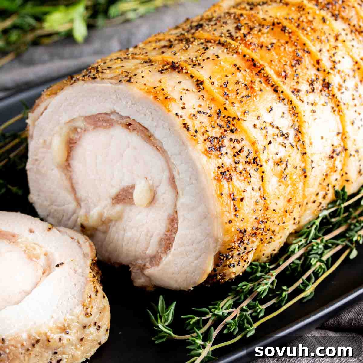 A perfectly roasted, moist and tender Provolone and Prosciutto Stuffed Pork Loin on a black plate, garnished with fresh thyme sprigs. This is a delicious keto and low carb dinner recipe, baked in the oven, perfect for your family this week!
