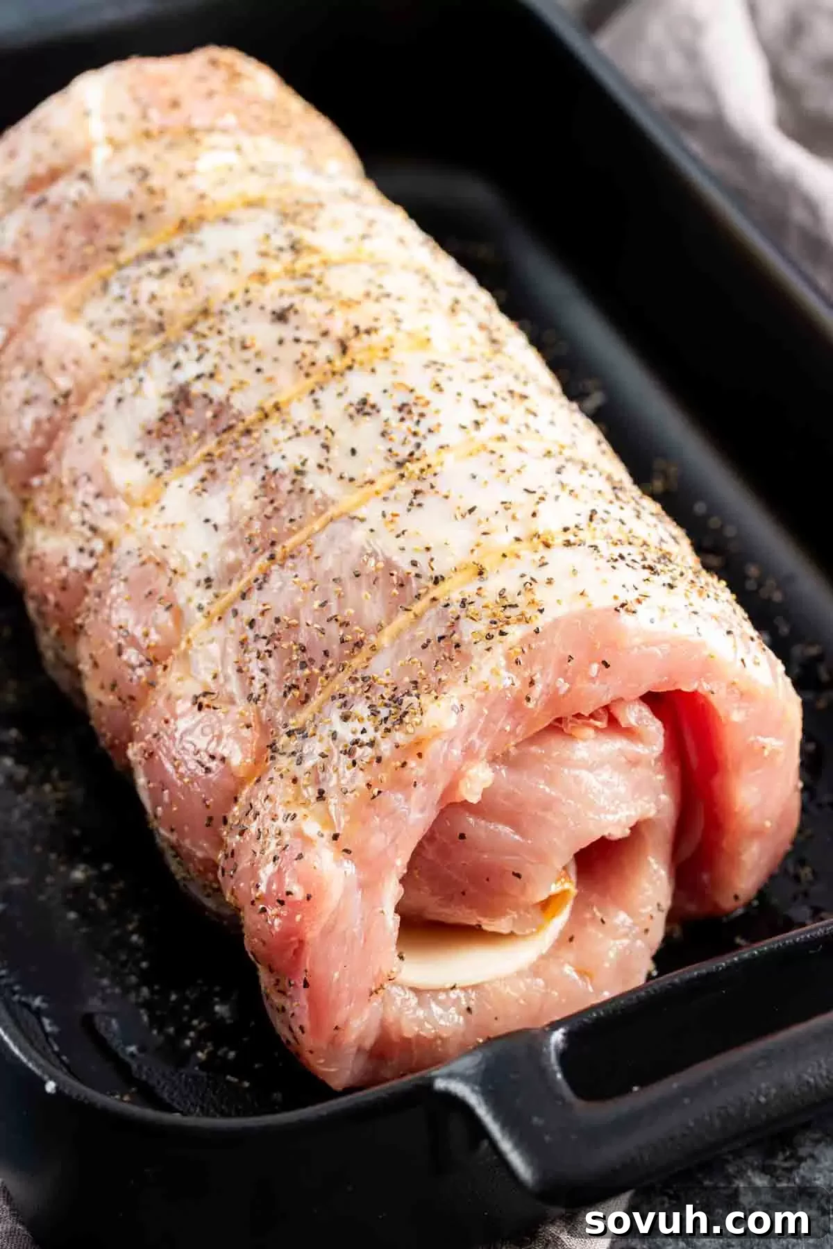 A tied Provolone and Prosciutto Stuffed Pork Loin resting in a baking pan, seasoned and ready for the oven. This shows the roast before it begins to cook.