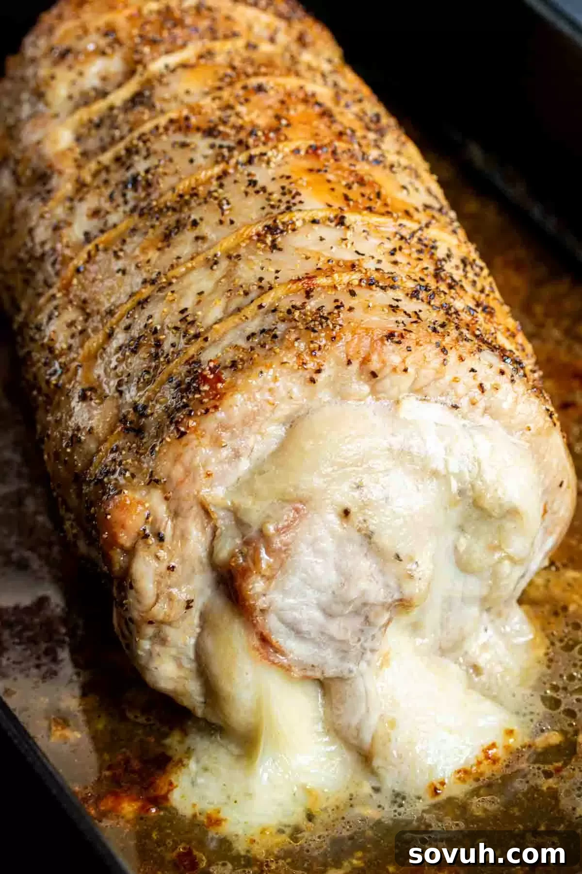 A beautifully roasted Provolone and Prosciutto Stuffed Pork Loin in a baking pan, garnished with fresh herbs, ready to be sliced. This highlights the golden-brown exterior and delicious aroma.