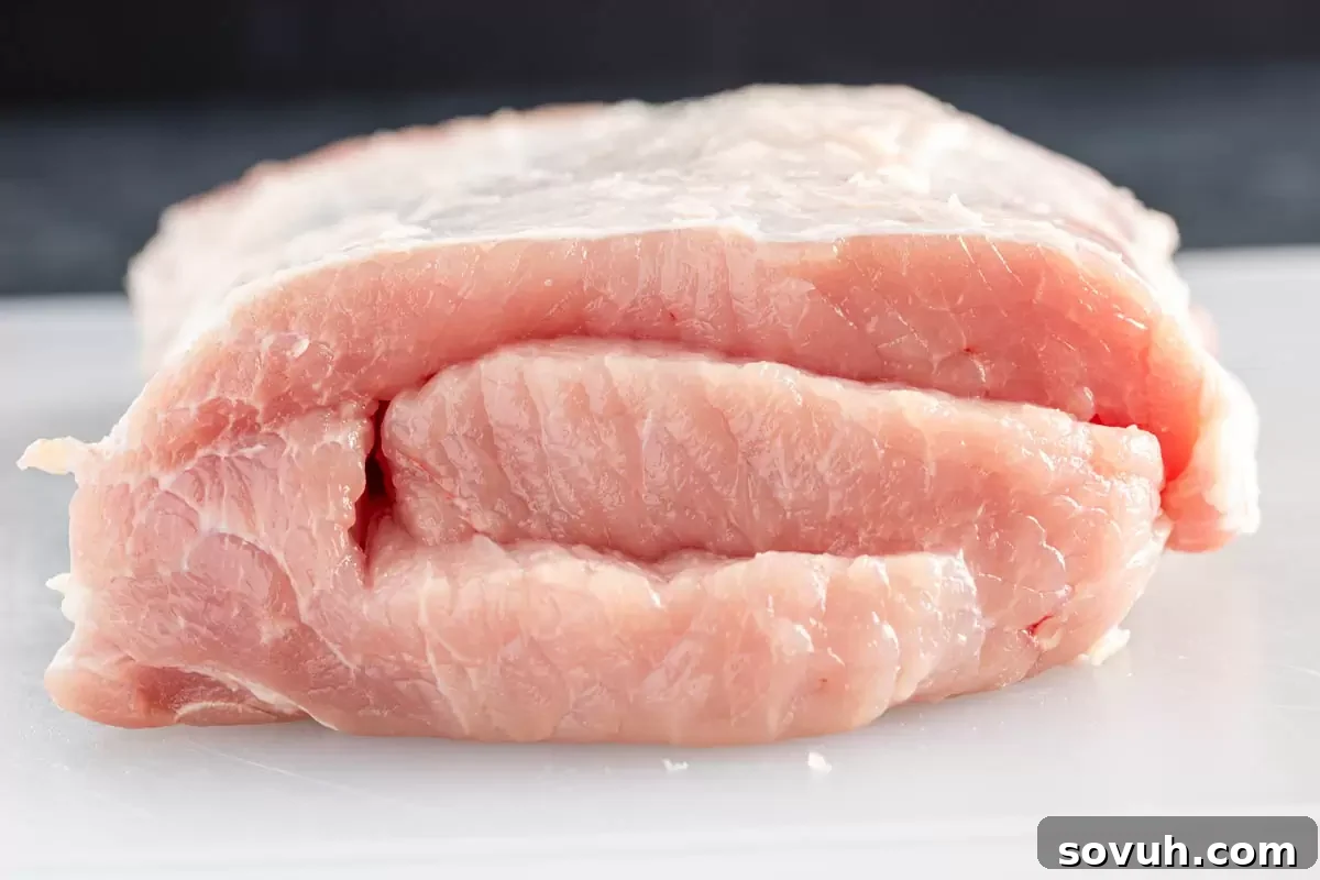 A raw pork loin on a cutting board, prepared for butterflying to make a stuffed roast. This visual shows the initial step of meat preparation.
