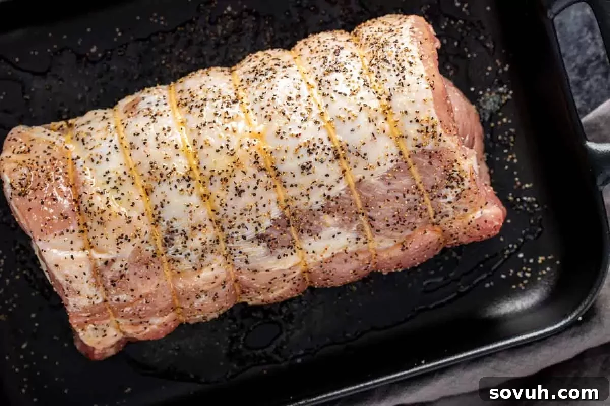 A seasoned Provolone and Prosciutto Stuffed Pork Loin, tied with butcher's twine, resting on a baking sheet with fresh rosemary, ready for roasting. This image highlights the preparation before cooking.