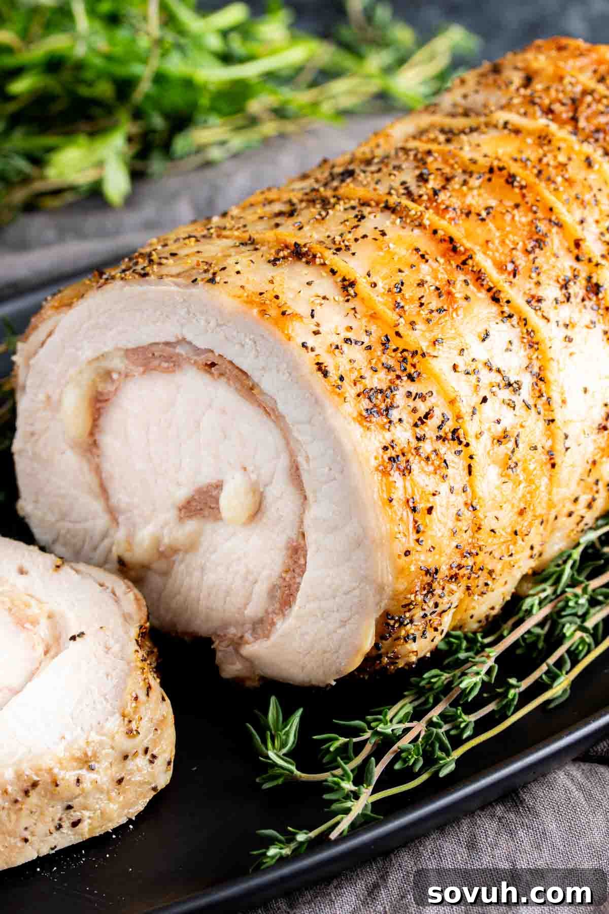 A sliced Provolone and Prosciutto Stuffed Pork Loin beautifully arranged on a black plate with fresh rosemary. This showcases the cross-section of the stuffed pork.