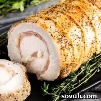 A Provolone and Prosciutto Stuffed Pork Loin on a black plate with thyme sprigs.