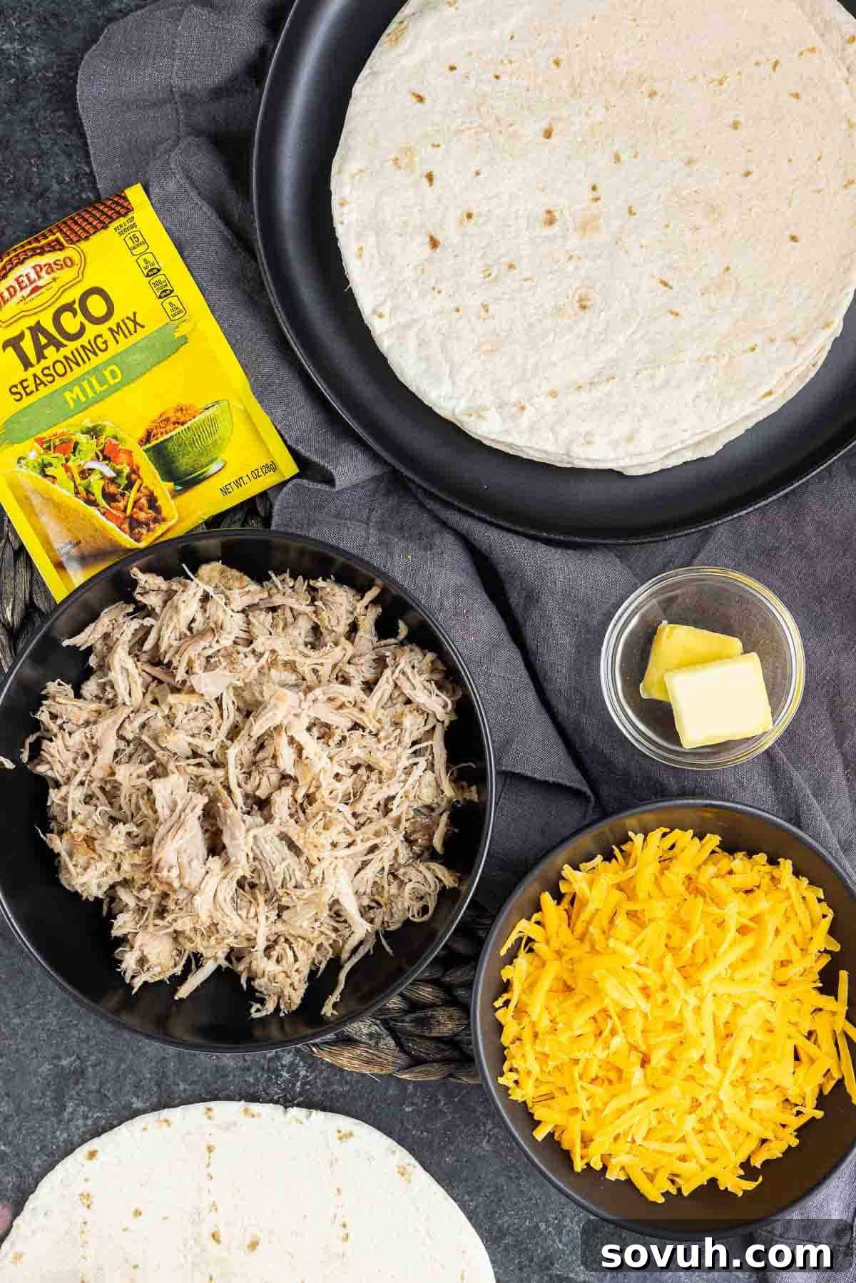 Ingredients laid out on a wooden board for making Pulled Pork Quesadillas, including tortillas, pulled pork, cheese, and fresh vegetables.