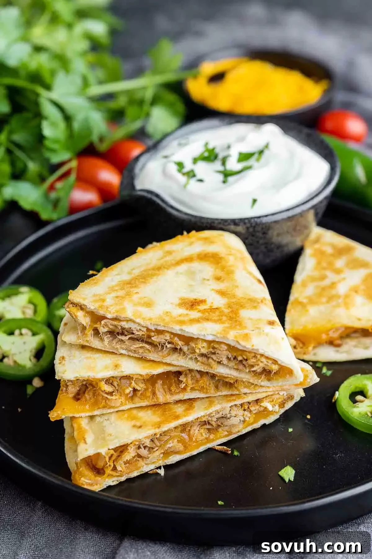 Pulled Pork Quesadilla on a black plate, garnished with a generous dollop of sour cream and a sprinkle of fresh herbs.