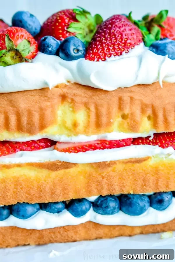 Close-up of a layered No Bake Red White and Blue Cake showing distinct layers of pound cake, whipped cream, blueberries, and strawberries. This easy dessert recipe is perfect for patriotic holidays and summer entertaining, featuring fresh ingredients and a simple assembly.
