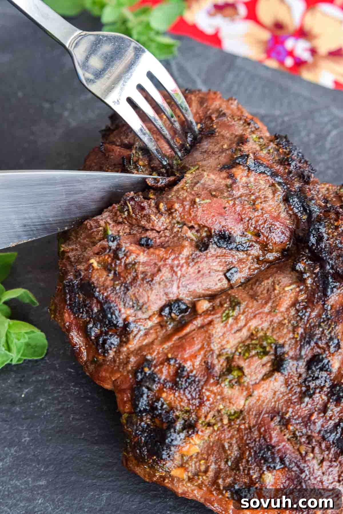 close up of knife carving herb crusted grilled leg of lamb
