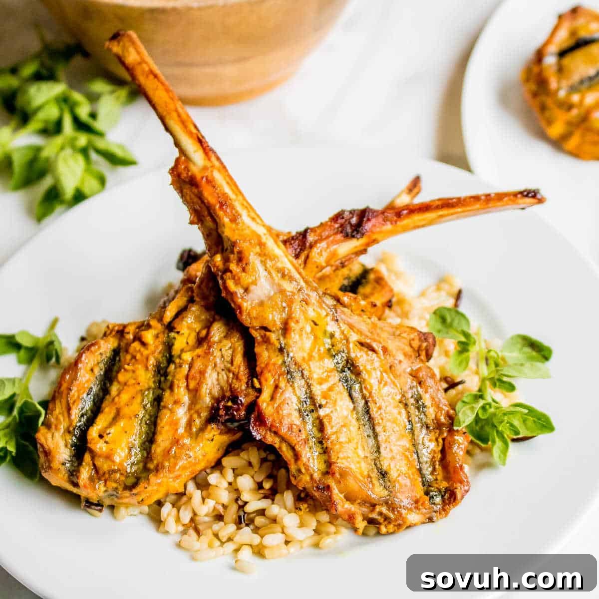 Two succulent Tandoori Grilled Lamb Chops served over a bed of fluffy brown rice, garnished with fresh herbs.