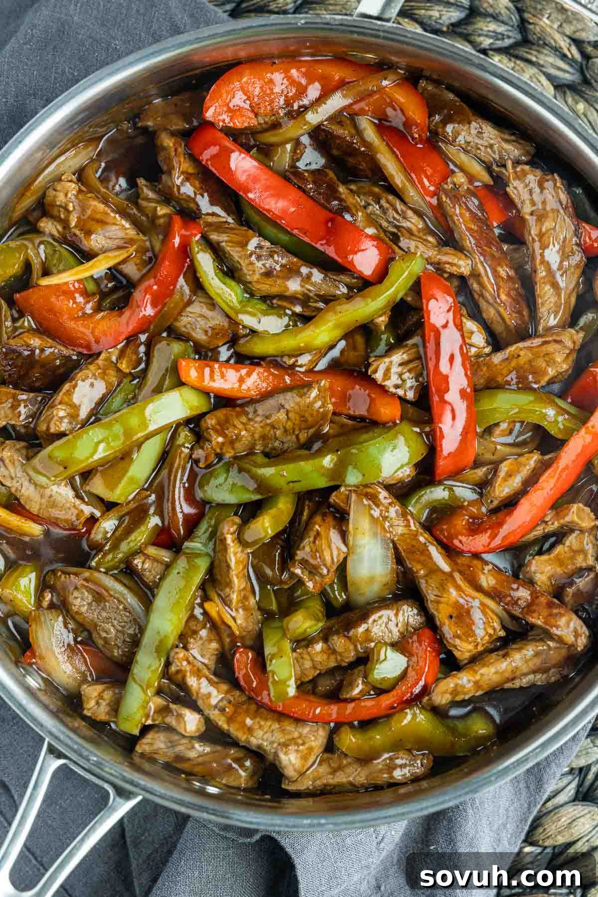 Close-up of Easy Pepper Steak cooking in a large skillet, showing beef and vegetables searing.