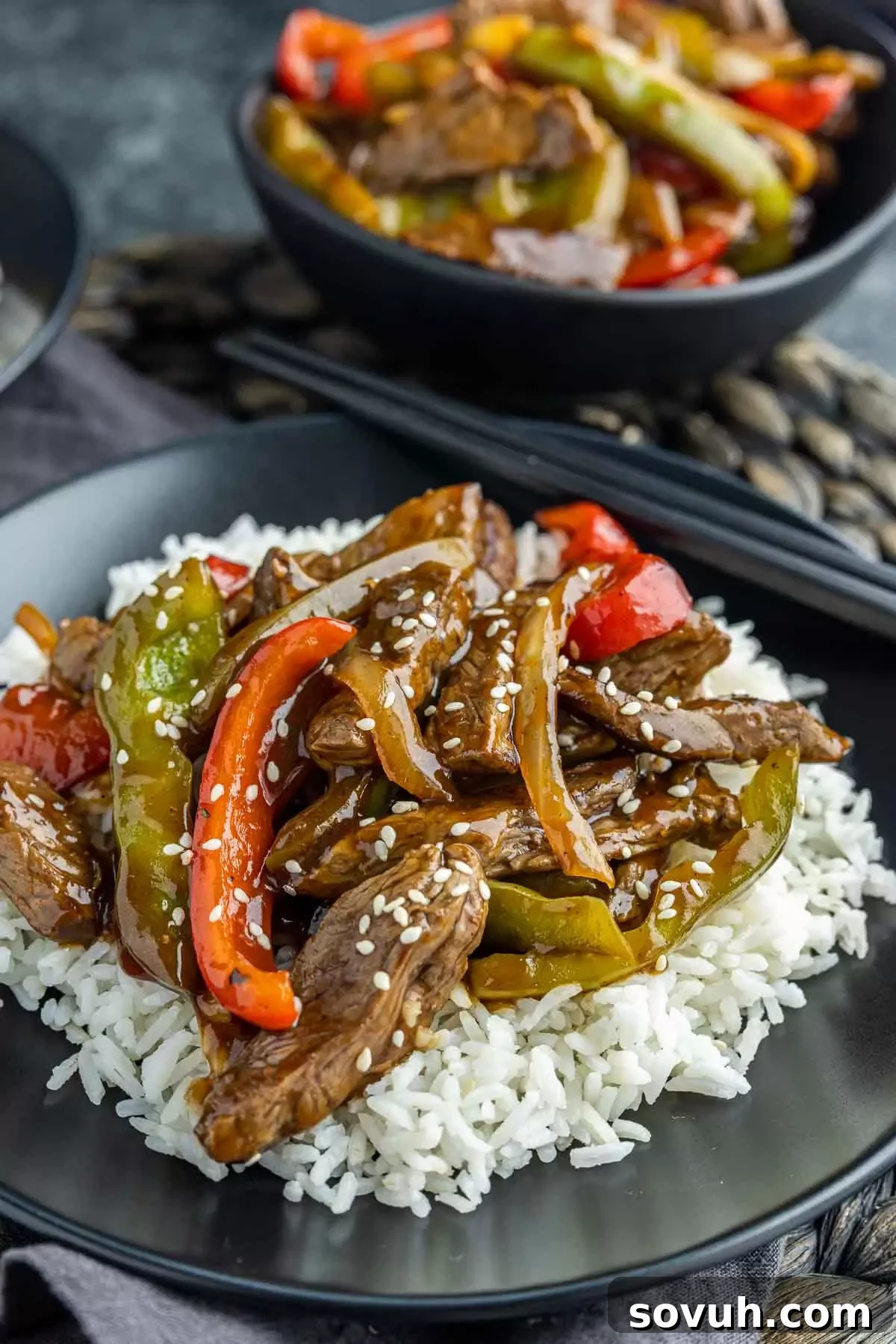 Easy Pepper Steak served on a sleek black plate with chopsticks, a bowl of additional pepper steak in the background.