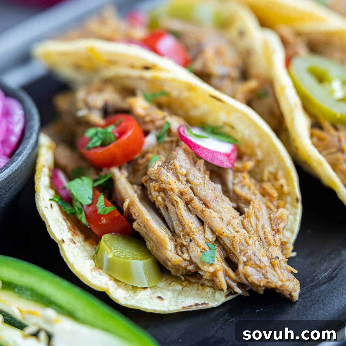 Irresistible Pulled Pork Tacos served on a sleek black plate, garnished with fresh cilantro and lime wedges