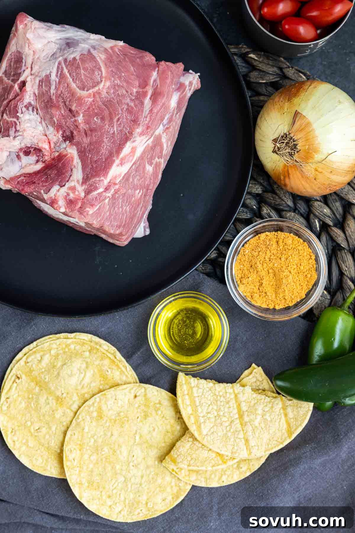 A vibrant display of ingredients for Pulled Pork Tacos, including a seasoned pork roast, sliced onions, and fresh corn tortillas