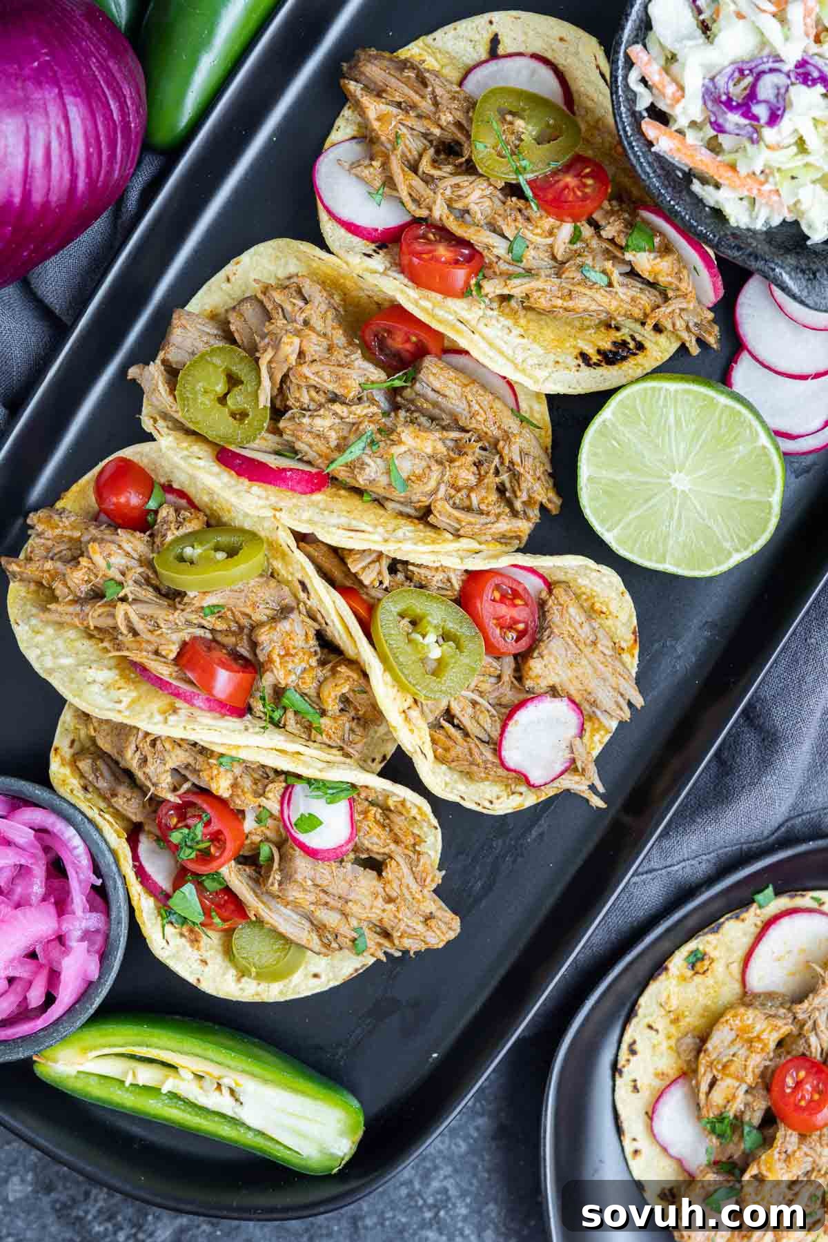 A stunning black platter showcasing an array of Pulled Pork Tacos, accompanied by a fresh side of coleslaw