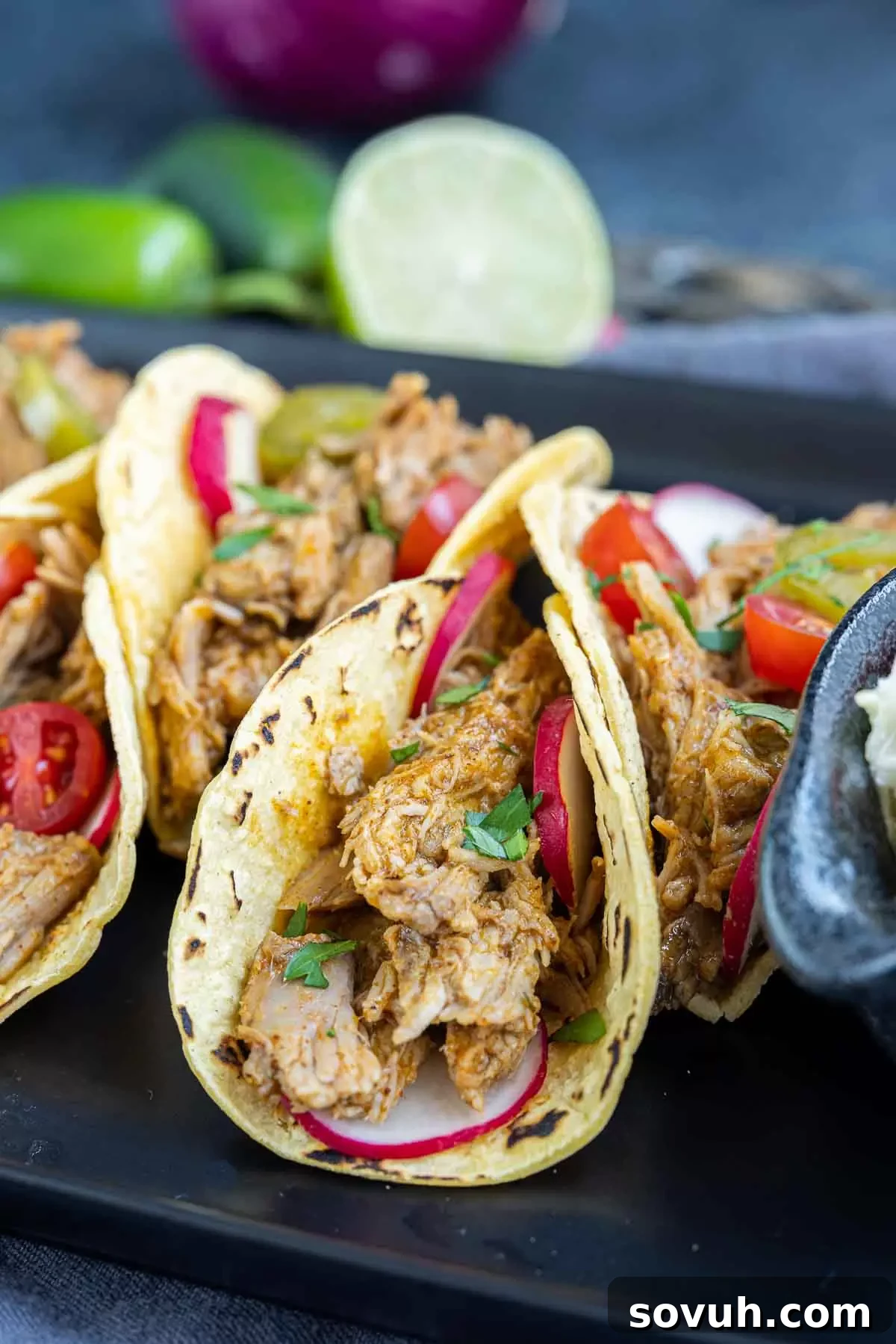 Close-up of freshly prepared Pulled Pork Tacos on a black platter, highlighting the rich fillings