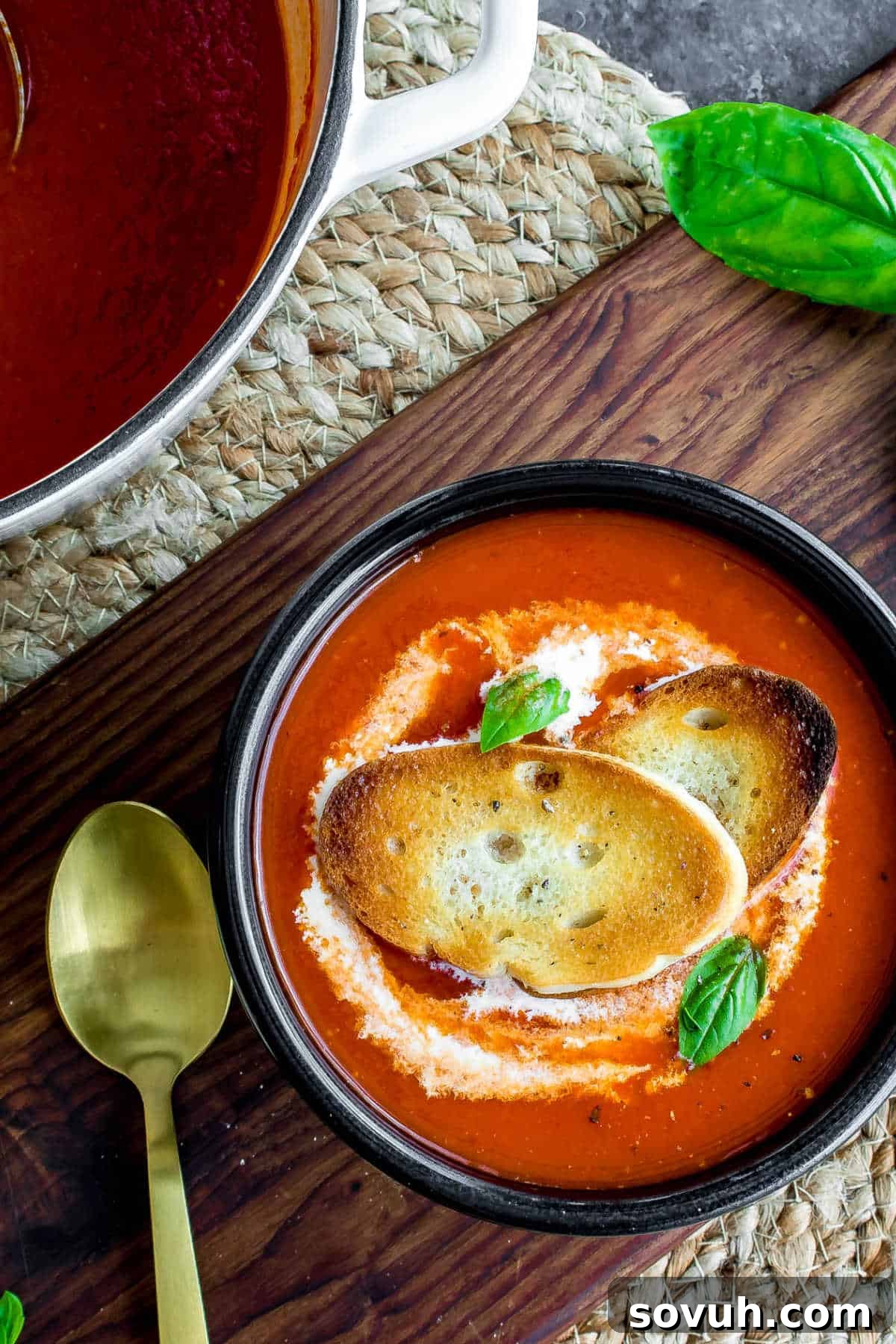 Roasted Red Pepper Soup in a black bowl with a gold spoon, garnished