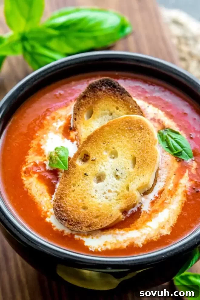 Roasted Red Pepper Soup in a black bowl with crostini and a spoon