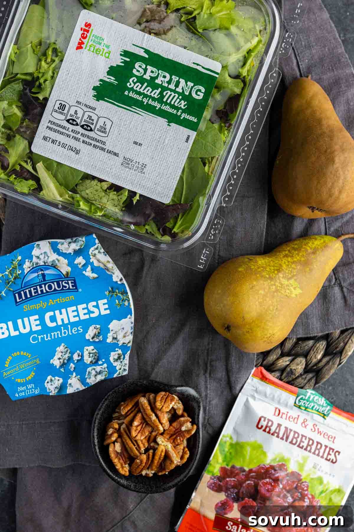 A collection of fresh winter salad ingredients including mixed greens, pears, pecans, dried cranberries, and blue cheese, ready for preparation.