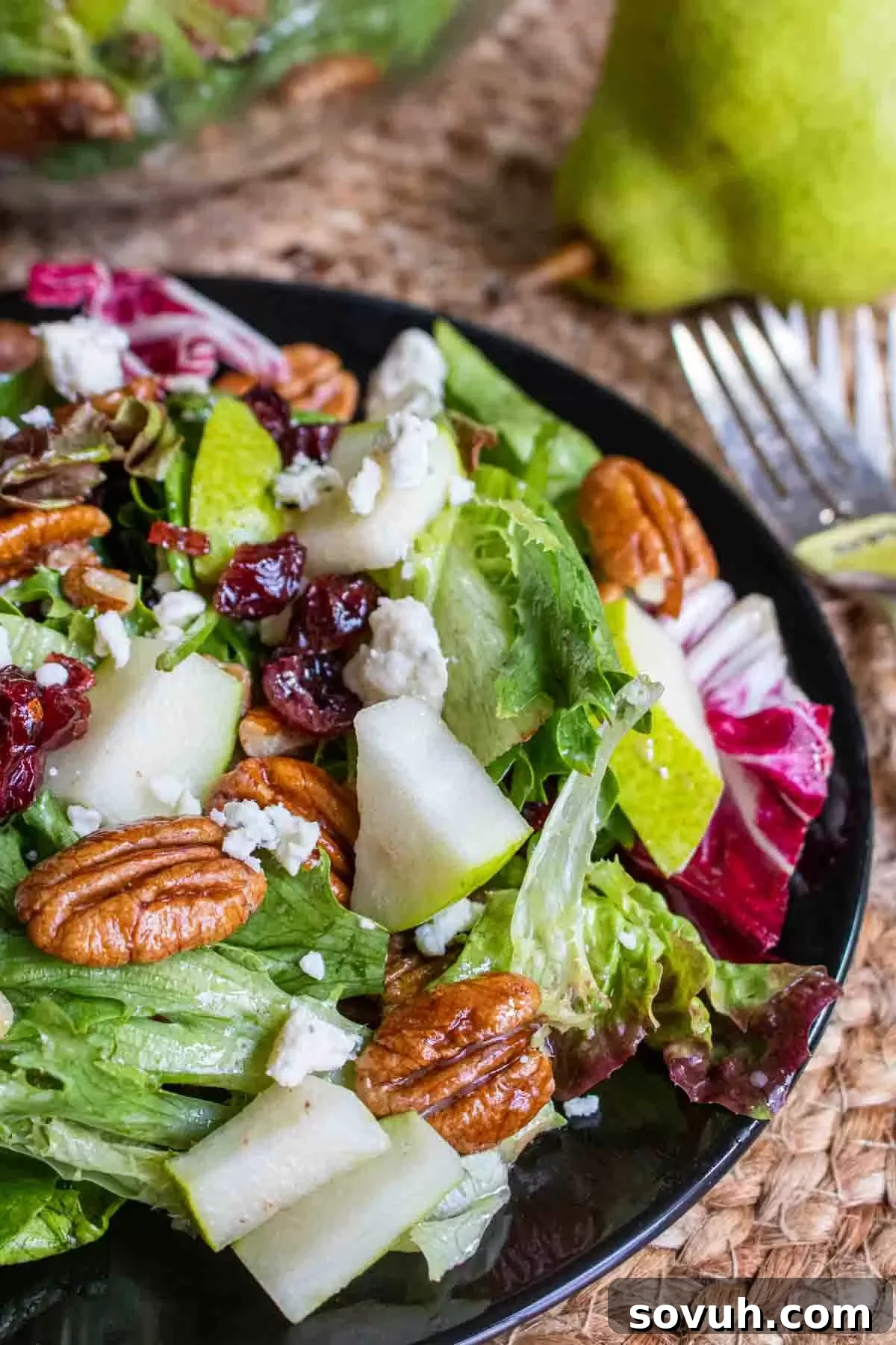 A close-up of the winter salad on a black plate, showcasing the vibrant colors of pears, cranberries, blue cheese, and greens.