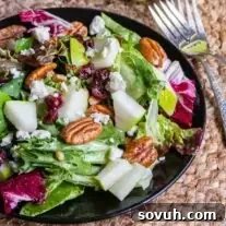 A vibrant winter salad with pears, cranberries, and pecans on a black plate, with forks ready to serve.