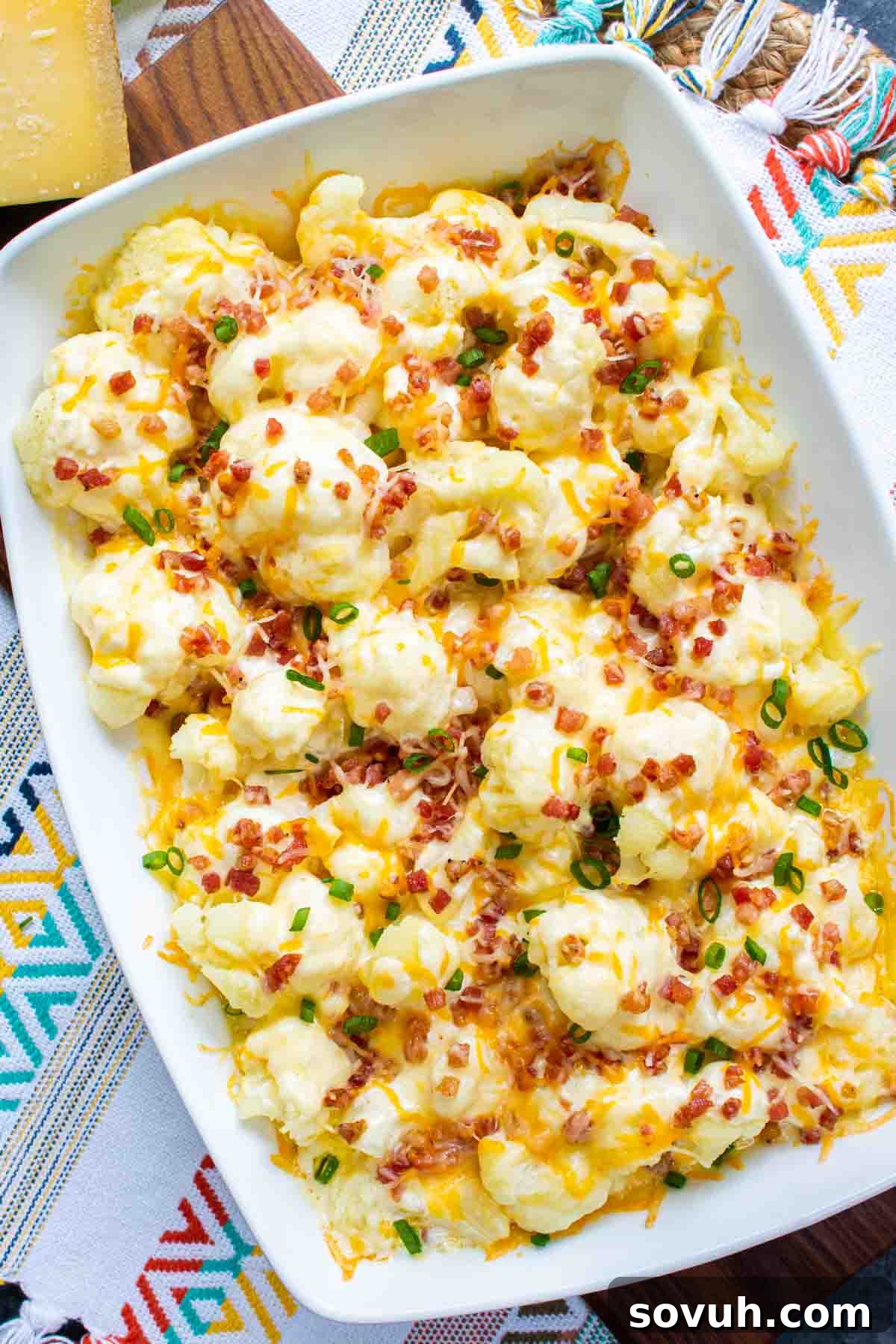 Cheesy sauce being poured over blanched cauliflower florets in a casserole dish