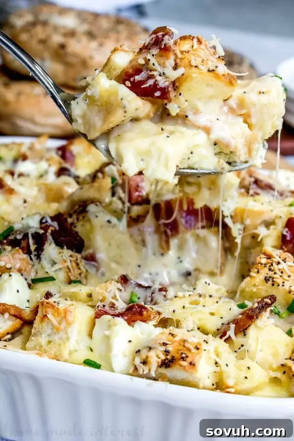 Close-up of a serving spoon dishing out a portion of Everything Bagel Breakfast Casserole, showcasing the bagel pieces, bacon, and melted cheese.