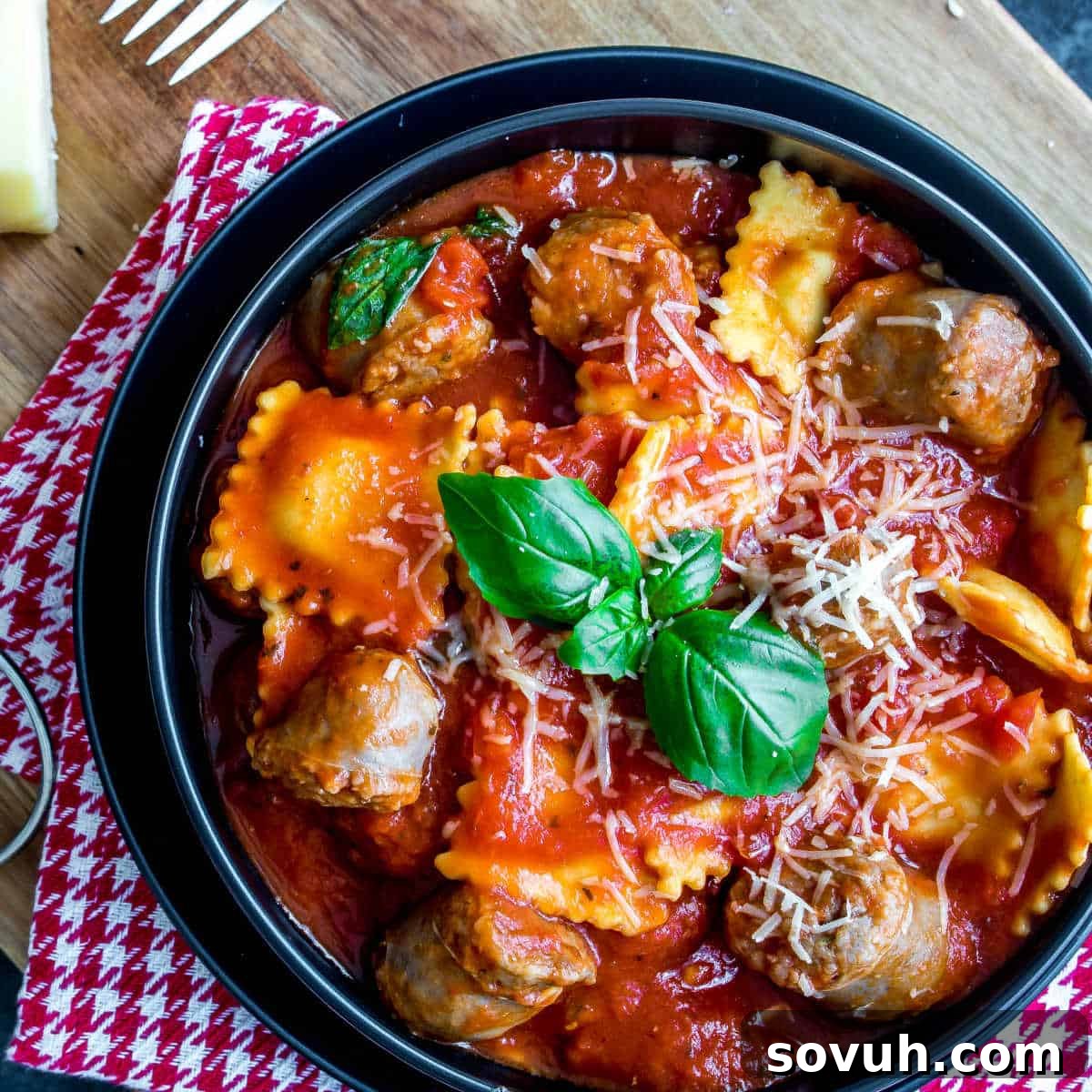 A vibrant bowl of Ravioli and Sausage Slow Cooker Casserole, garnished with fresh basil and Parmesan cheese.