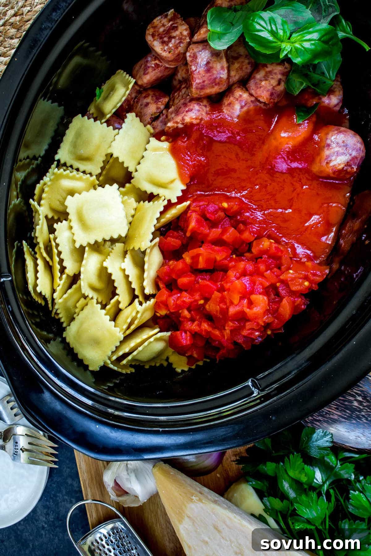 A crock pot filled with the colorful raw ingredients ready to slow cook into a delicious Ravioli and Sausage Casserole.