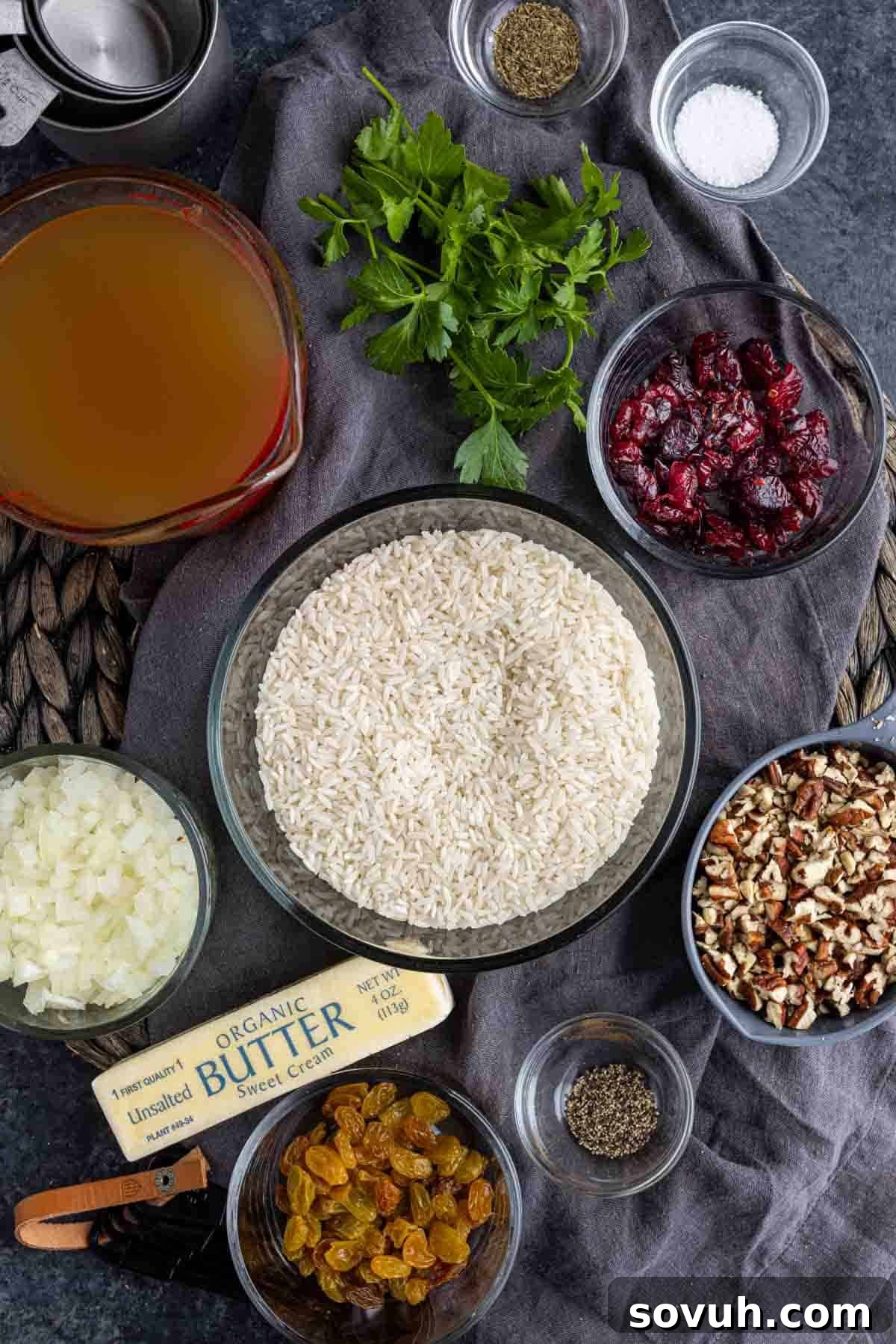 A flat lay of fresh ingredients for Pecan Rice Pilaf, including rice, pecans, onion, butter, and herbs.