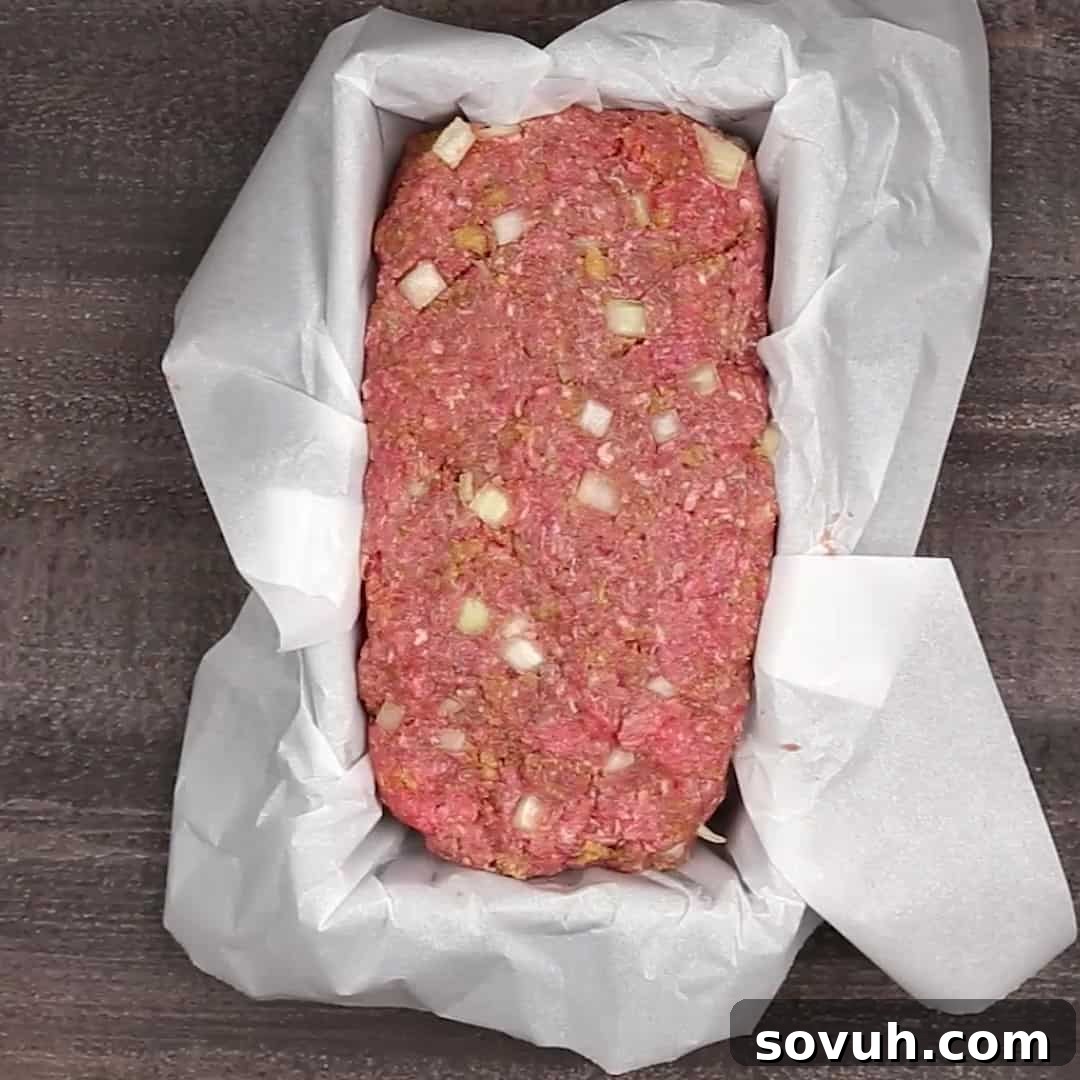 keto meatloaf in parchment paper lined loaf pan on a wooden table.