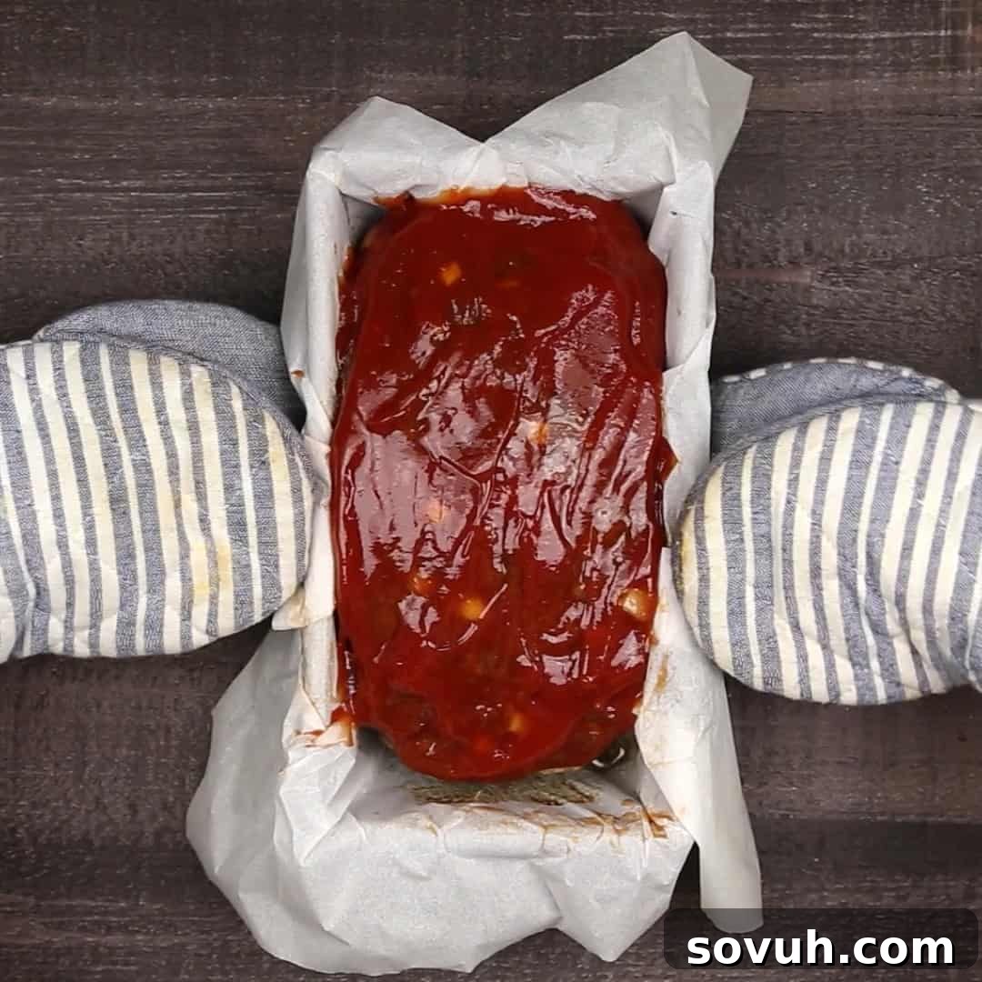 keto meatloaf in parchment paper lined loaf pan with two hands holding it.