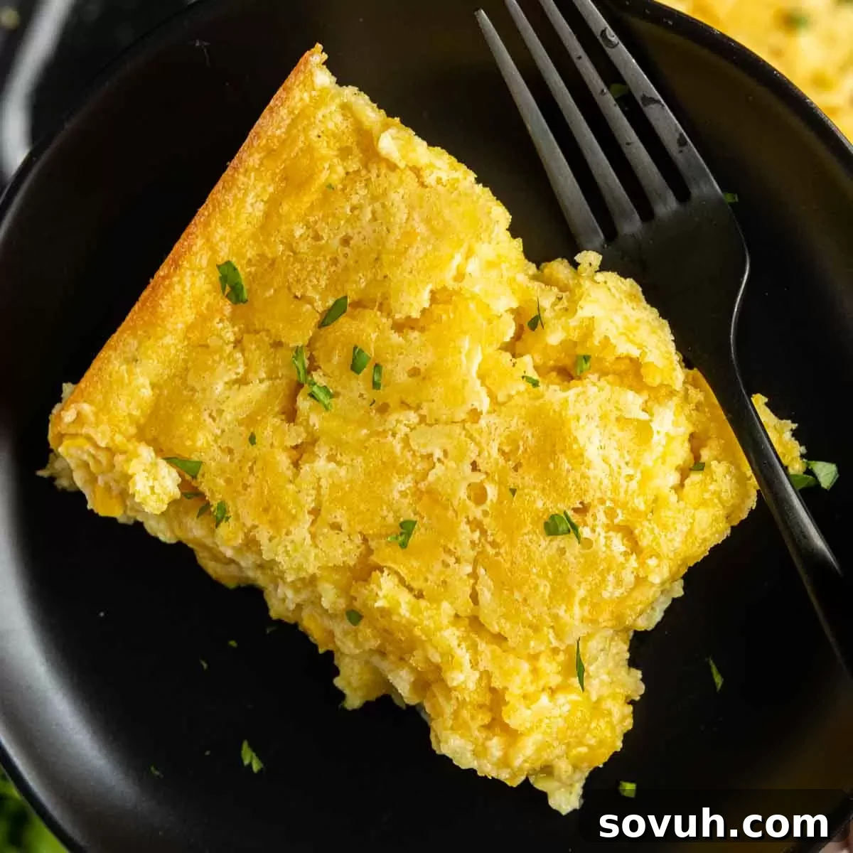 holding a plate of Creamed Corn Casserole with a black fork
