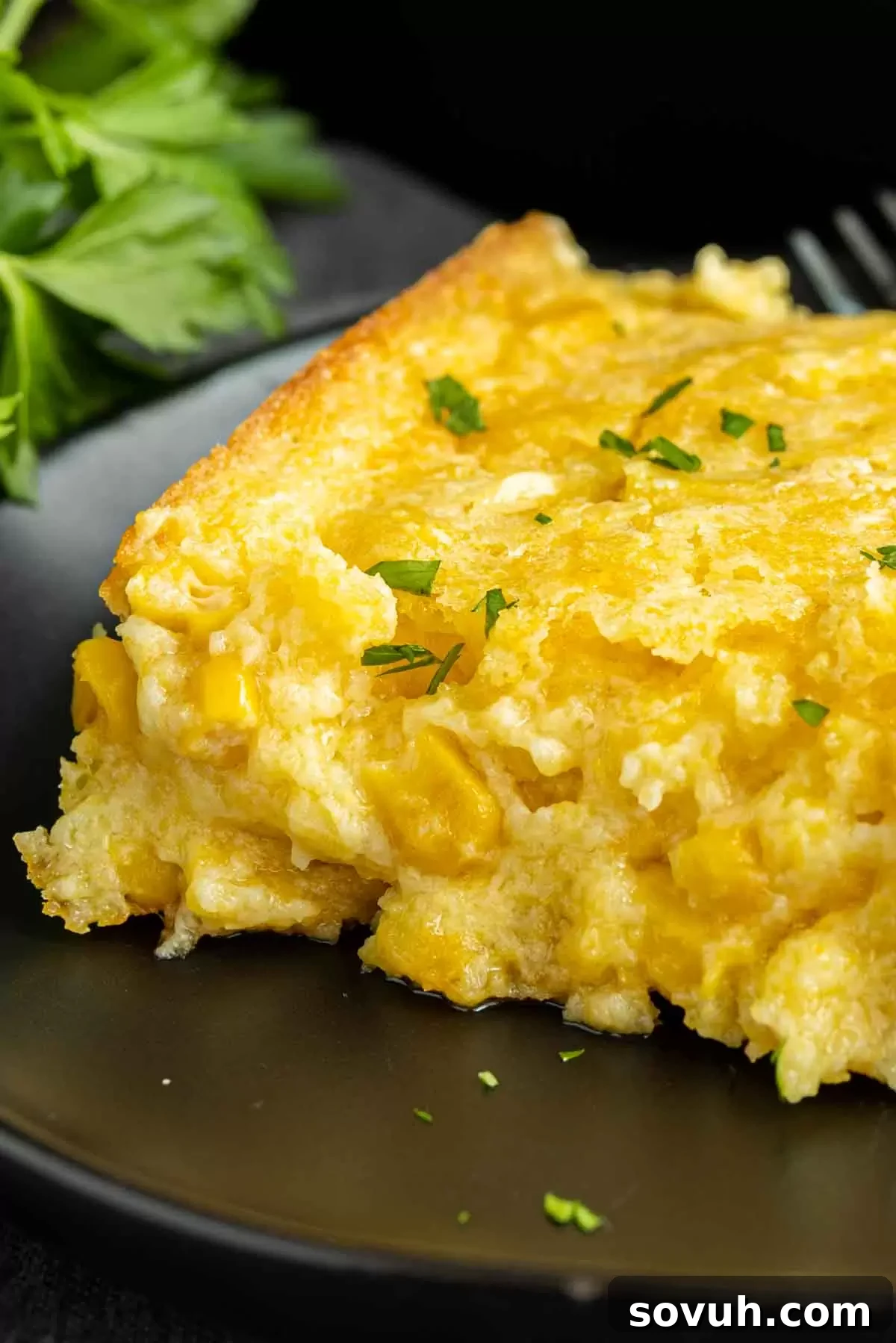 Creamed Corn Casserole on a black plate garnished with parsley